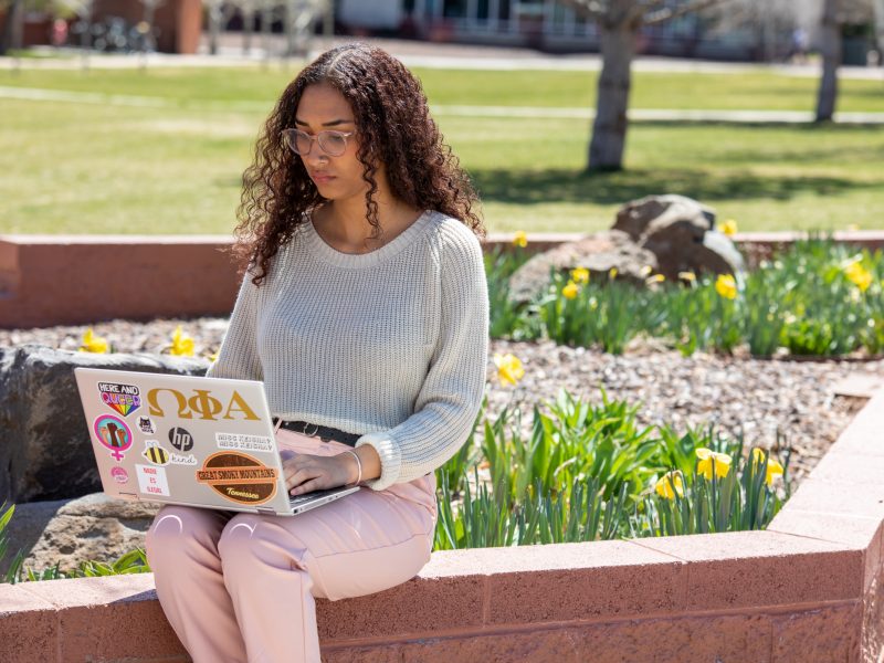 A photo of a student working on a laptop outside on a sunny day at Flagstaff campus.